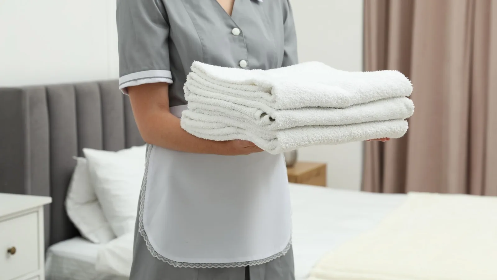 Cleaner holding folded white towels in bedroom